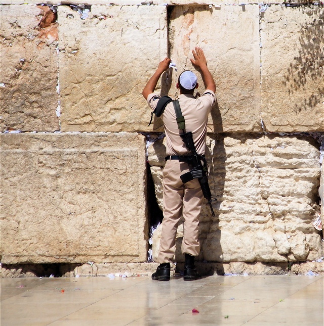 Soldier at Wailing Wall prays with his gun.